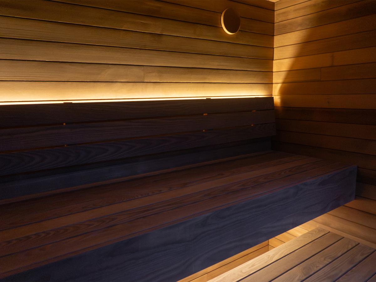 Wood benches and backrest with concealed lighting and a round wall vent inside the Ember Cabin sauna.